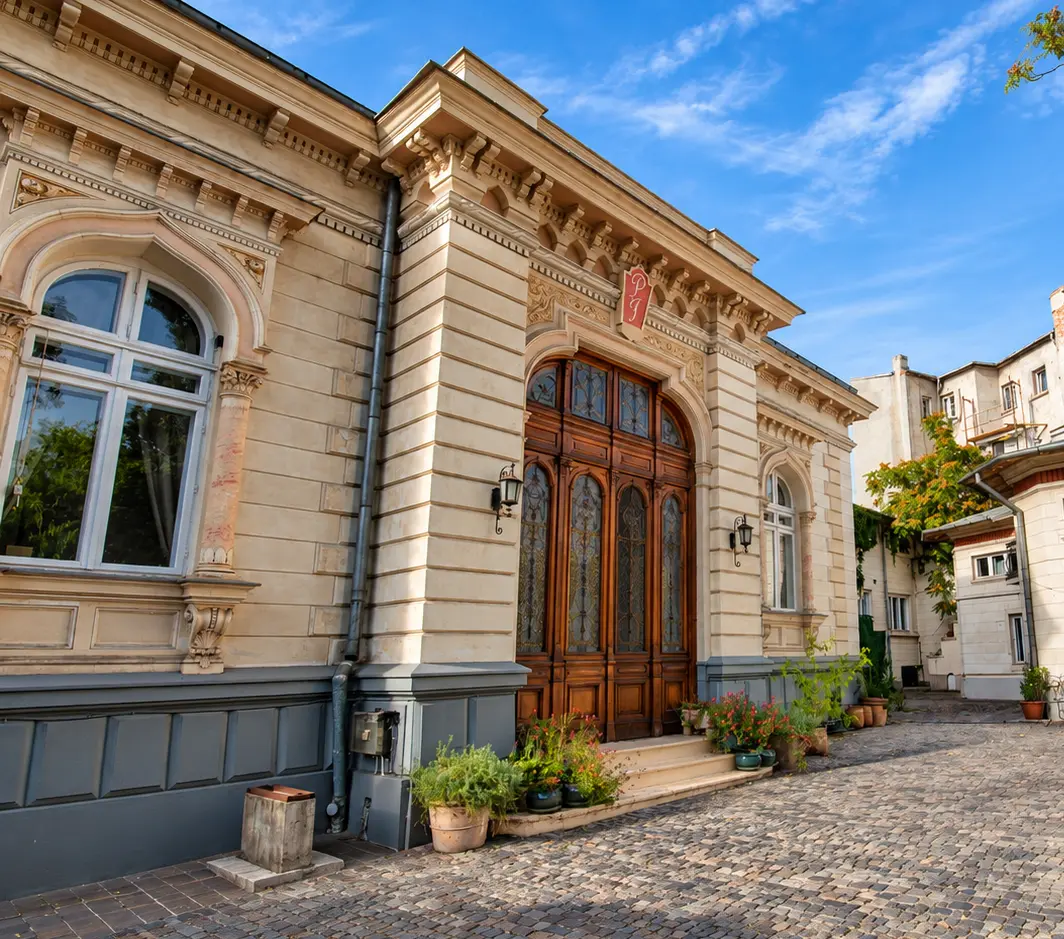 Vedere din colț spre fațadă și intrare, cu aleea pietruită care duce spre curte