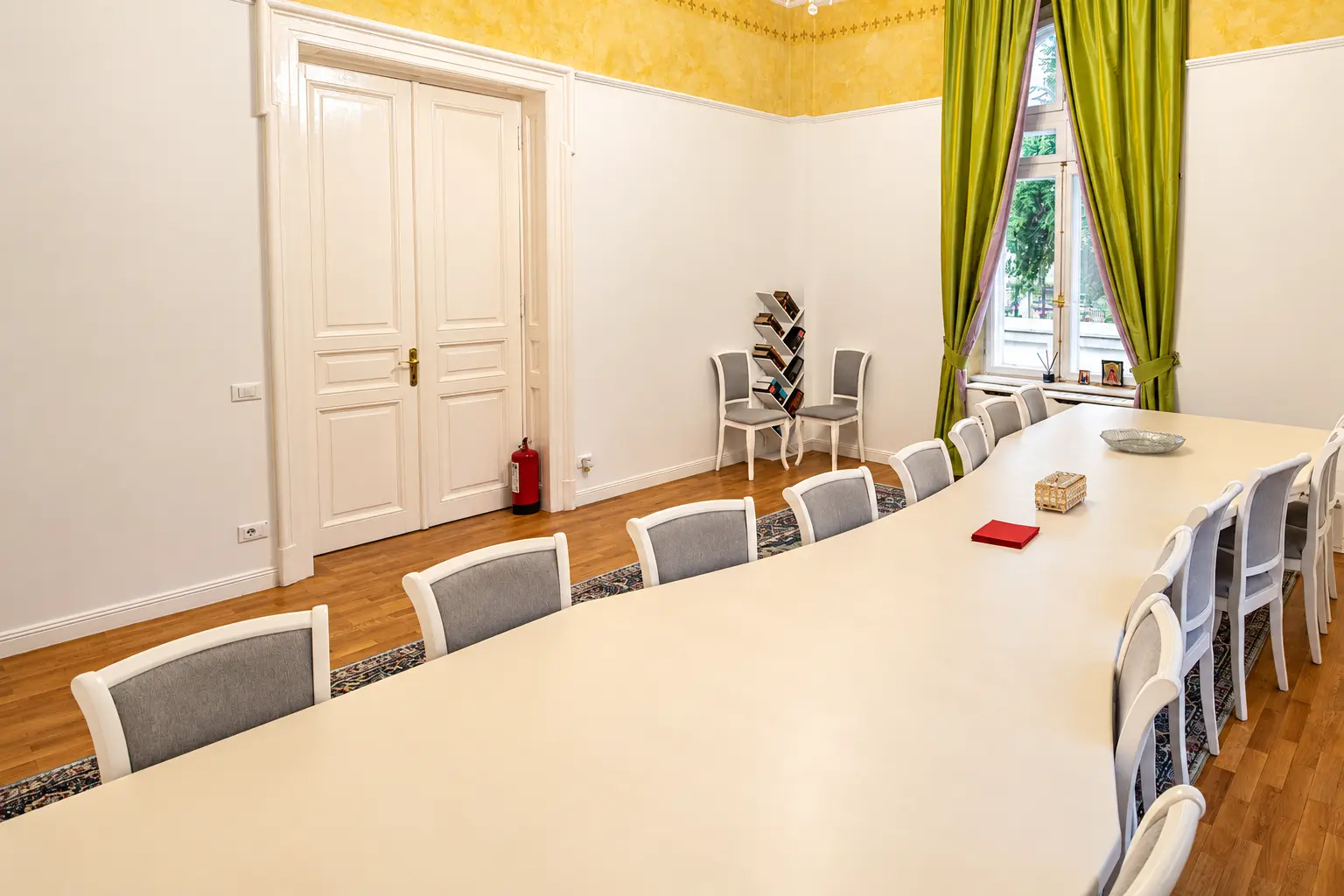 A meeting or hearing room with a long table and tall windows for 22 people