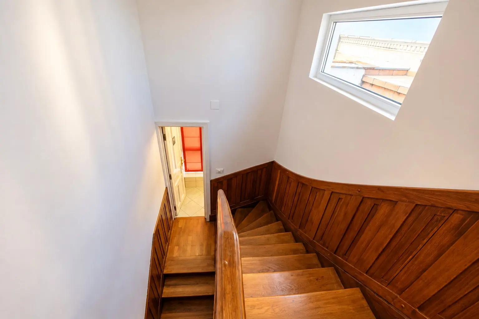 A wooden stairwell with a sunlit landing