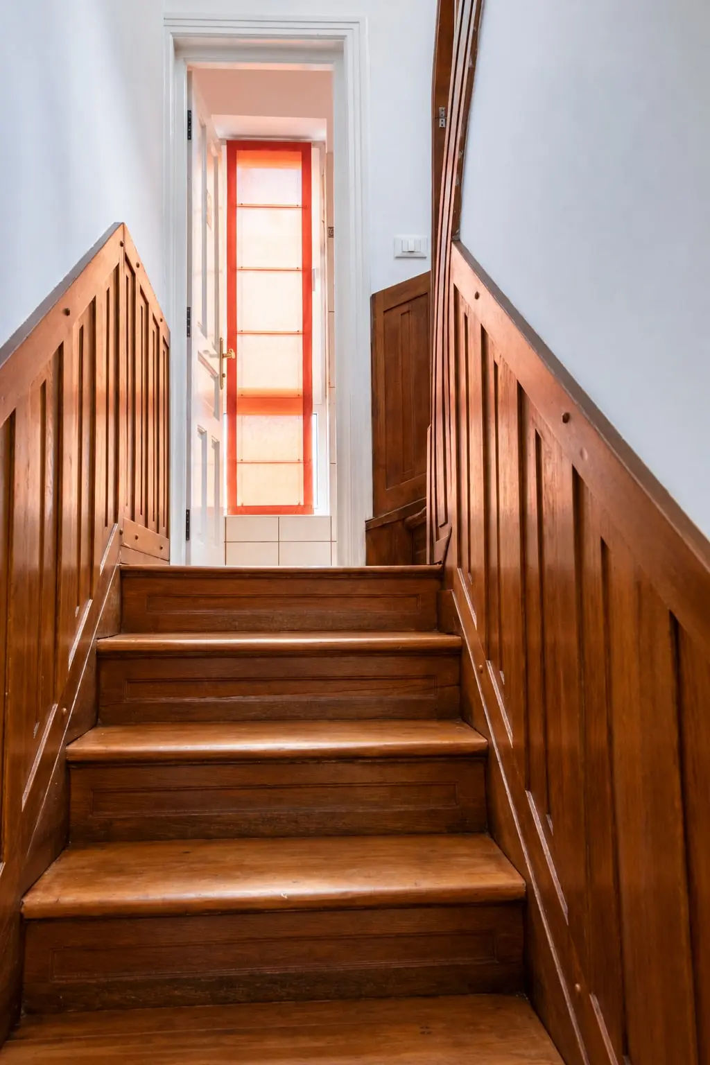 A wooden stairway to a sunlit landing