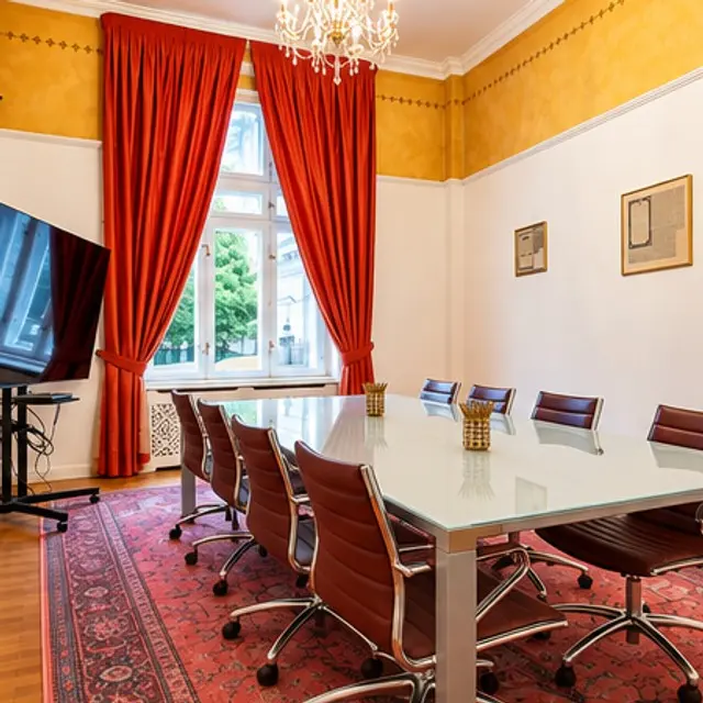 Boardroom with a glass table, red curtains and a chandelier